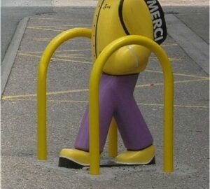 Barrière CONVIVIALE jaune autour d’un petit piquet violet et ballon noir, sur sol gris près d’un banc et marquages au sol.